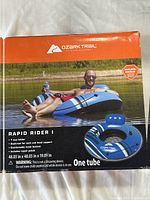 Box showing Ozark Trail Rapid Rider I inflatable tube with cup holder and backrest on water. Features and dimensions visible.