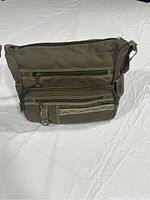 Front view of the olive green canvas shoulder bag showing multiple zipped pockets and adjustable strap on white background.