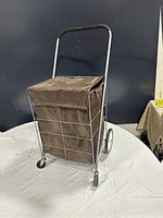 Brown fabric shopping trolley with metal frame and 4 wheels, shown with flap closed