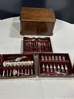 Wooden box and three velvet-lined trays with assorted stainless flatware including forks, spoons, and serving utensils.