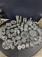 Wide view of the entire collection on a black table showing variety of crystal dinnerware pieces including plates, bowls, glasses, decanters, and serving dishes arranged for display.
