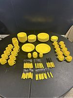 Full set of yellow Mikasa ceramic dinnerware, flatware laid out on a black table, showing quantity and color