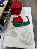 Full set of red Santa coats, green pants, red and white hats, and white synthetic beards laid out showing condition and completeness.