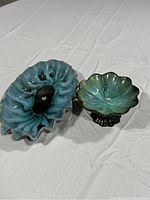 Two ceramic serving dishes with floral-shaped scalloped edges, blue and green glaze, side by side on a white cloth surface.