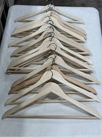 Top view of 14 vintage wooden hangers stacked in two rows showing the smooth natural wood finish and metal hooks.