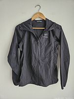 Front view of black Arc'teryx jacket hanging on a wooden hanger.