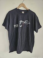 Black Canon EOS System T-shirt, large size, hanging on wooden hanger, front view showing camera graphic.