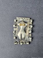 Front view of a rectangular handmade brooch with an abstract human figure and star engravings on top border.