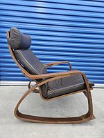 Side angle showing the curved wooden frame and padded leather seat with headrest