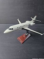 White metal model airplane displayed on a wooden base labeled 'MARQUIS JET', angled front view showing windows, engines, and tail fins.