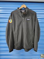 Full front view of a black Patagonia jacket with zipper and Firefox logo patch on left sleeve.