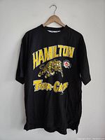 Full view of black vintage Hamilton Tiger-Cats t-shirt with yellow text and tiger graphic on front.