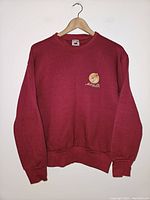 Front view of maroon vintage sweatshirt on hanger showing small embroidered front left chest logo.