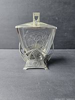 Frontal view of the vintage WMF cookie jar showing the cut glass container with Art Nouveau etched design inside a silverplated frame with hallmark and decorative handle on top.
