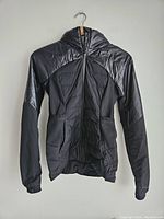 Front view of a women's Lululemon black jacket with quilted sections, front pockets, hood and elastic cuffs.