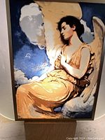 Full view of the miniature glass sun catcher showing an Art Nouveau style angel with golden dress and wings, blue cloudy sky background framed in brown.