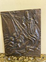 Front view of bronze plaque showing Saint Nikolaus blessing four children emerging from water with waves. Inscription 'SANKT NIKOLAUS' visible at lower right.