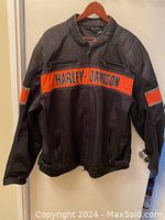 Front view of the Harley Davidson motorcycle jacket with black and orange color scheme, showing brand name across chest and overall construction.