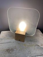 Frontal view of the table lamp illuminated, showing frosted glass diffuser and natural wood base.