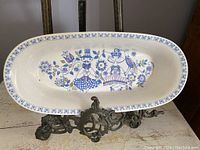 Top view of oval ceramic serving dish decorated with blue, purple, and olive green Mid Century stylized figures and floral pattern.