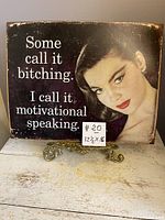 Tin advertising sign with distressed edges and partial image of a woman, showing text 'Some call it bitching. I call it motivational speaking.'