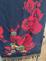 Close-up of black shawl with red floral pattern and fringe.