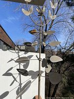 Overall view of the tall vintage iron garden sculpture outdoors against a white wall and tree background.