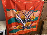 Full view of the scarf spread flat showing floral design with yellow flowers and red background with green and purple elements.