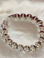 Full view of the circular silver tone bracelet laid on fabric, showing the spherical beads with rhinestone stripes and clasp.