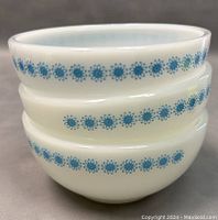 Stacked view of three white milk glass cereal bowls with a blue daisy pattern around the rim.
