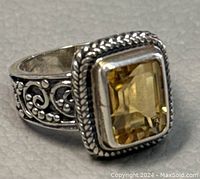 Close up image of rectangular yellow gemstone set in a detailed 925 sterling silver ring with hand-etched and beaded designs.