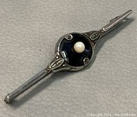 Close-up photo of the front top side of the brooch to show pearl and decorative details on black background