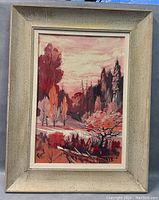 Full view of framed landscape painting with autumnal trees and a pink sky on board.
