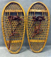 Front-facing image of pair of Bear Paw traditional snowshoes side by side showing full wooden frames and woven webbing with leather straps.