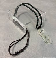 Jade Buddha pendant hanging from braided cord, showing pendant detail and cord texture.