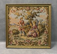 Framed Aubusson tapestry depicting young man and woman in outdoor romantic scene, showcasing the entire tapestry with ornate floral border and background landscape.