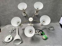 Mid century modern chandelier with five white cone shades and mid century modern clip-on table lamp with white shade and clip base laid out together with cords and power plugs visible.