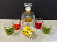 Photo showing 5 retro bowling/curling shot glasses with color graphics and vintage Drambuie decanter bottle with stopper on a white surface against black back drop.