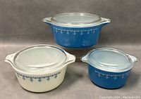 Three Pyrex lidded casserole bowls (two blue, one white) arranged side by side showing exterior design and lids.