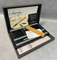 Sheaffer calligraphy set opened showing fountain pen, ink pot, multiple nibs, and instructional booklets inside.