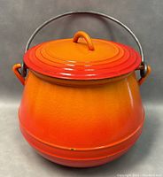 Front view of flame red enameled cast iron bean pot with lid and metal handle