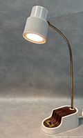 Full view of vintage reading lamp with white cylindrical shade, brass goose-neck, wooden accent base, and power cord, lit and working.
