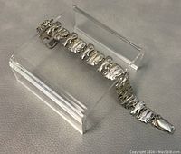 Full view of the silver plated cat link bracelet laid on a grey fabric background with clear stands for support.