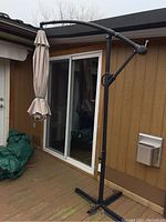 Full view of cantilever patio umbrella folded and bolted to wooden deck with sliding door in background.