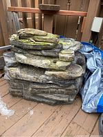 Front and side view of a heavy decorative rock fountain with realistic textured rock layers and moss appearance