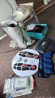 Photo showing the resin shower stool, foam walker boot, Goldline curling shoes in box, ankle weights, Dr Ho's circulation promoter device with pads and wires, and additional accessories scattered on floor.