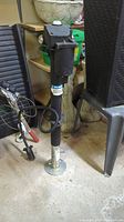 Full view of the hydraulic jack standing vertically on a concrete floor near assorted items.