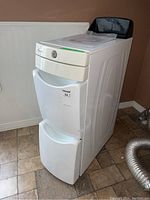 White tall laundry organizer tower with three drawers and black tray top on tiled floor.