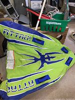 Green and blue inflatable water tube with 'Attack' logo and blue straps laid on the floor
