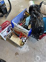 Photo showing various painting and preparation supplies arranged in pails and plastic totes, including the spray gun box.
